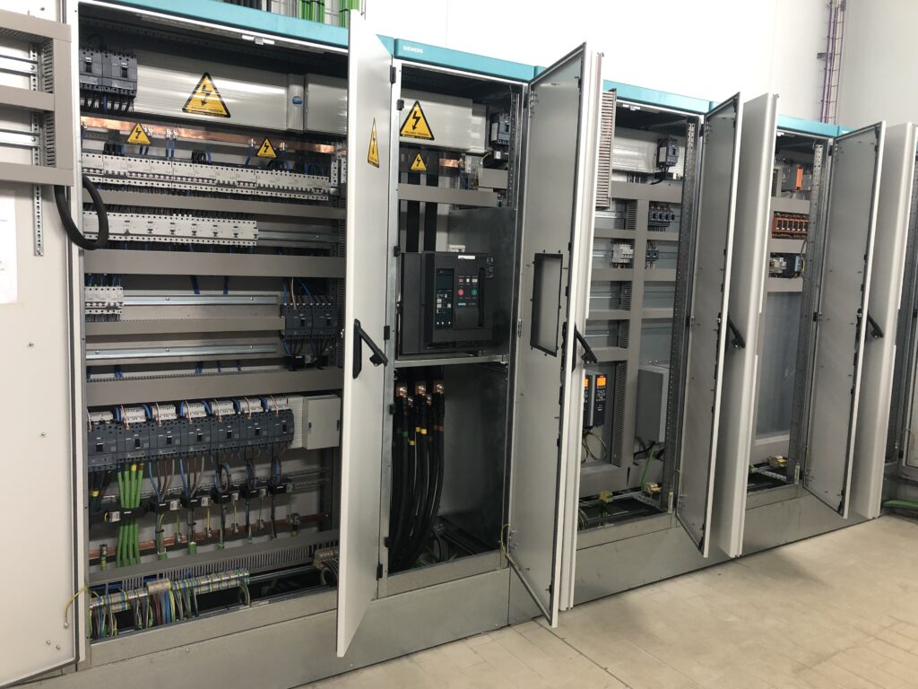 Row of electrical cabinets with their doors open: circuit breakers, terminal strips, control wiring and a main power switch