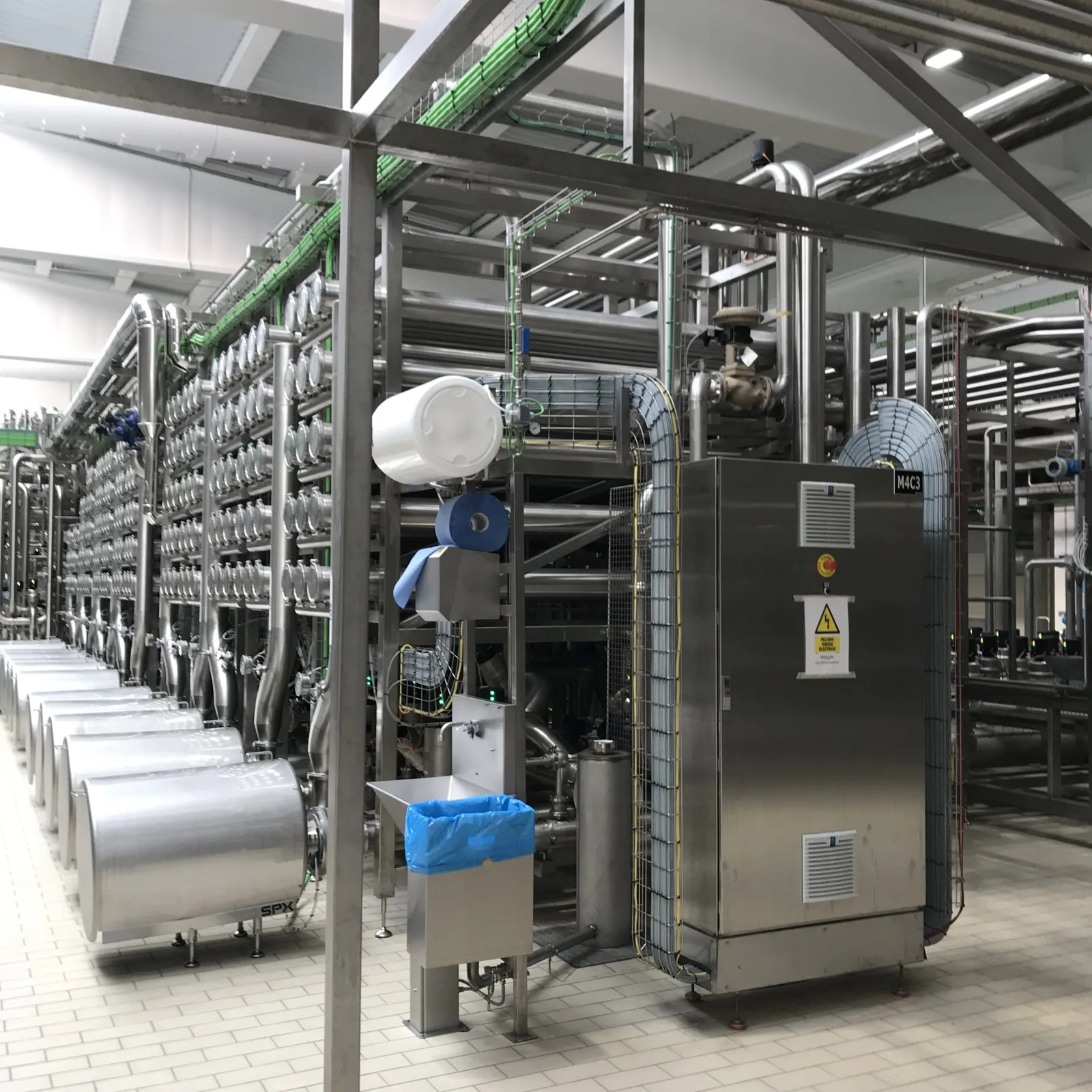 Stainless steel electrical panel with an emergency stop button, next to a line of stainless steel pipework and pumps in a food plant