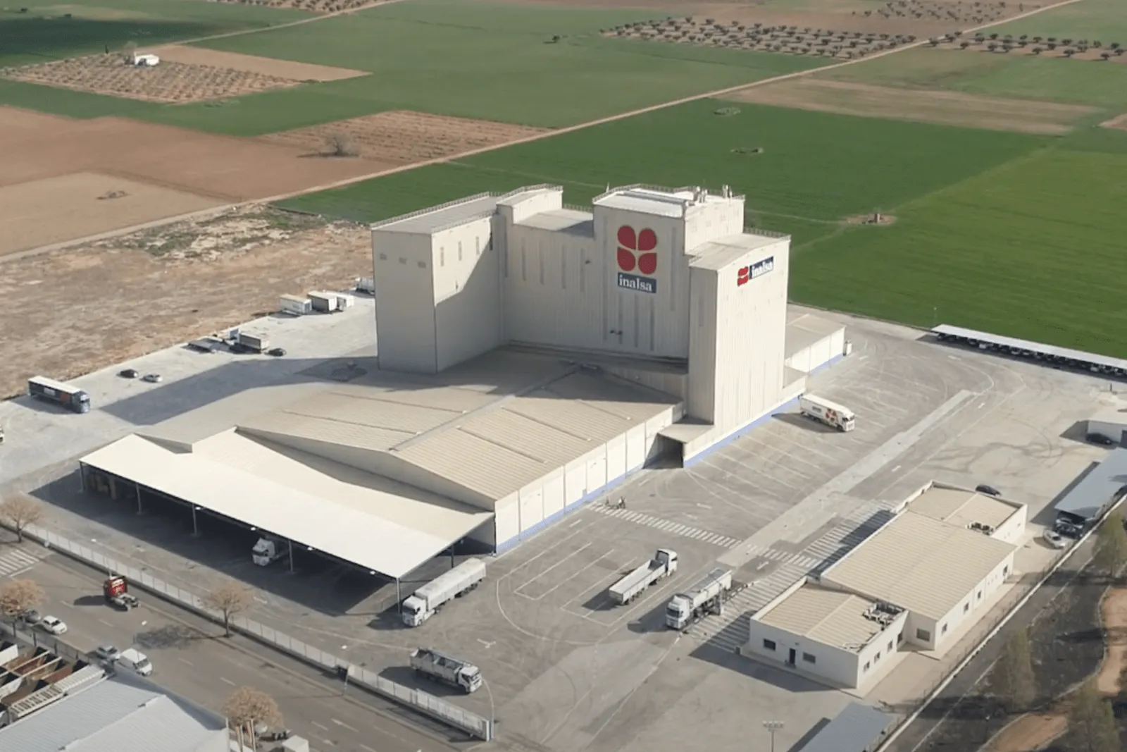 Aerial view of Inalsa's feed mill: production tower with the company logo, storage buildings, bulk feed tanker trucks on the yard and farmland all around