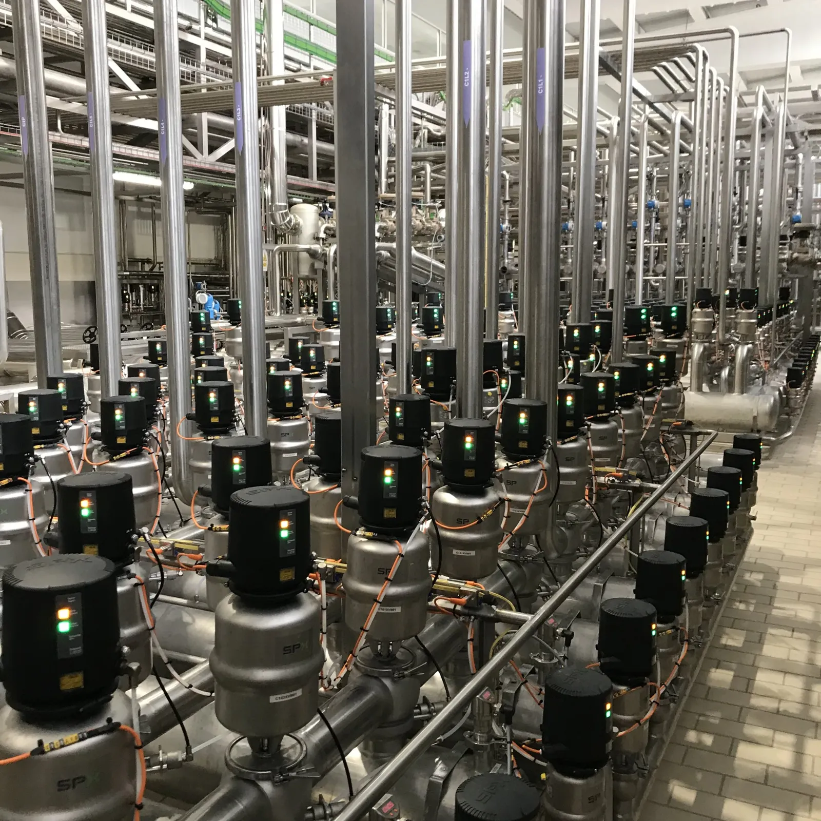 Bank of stainless steel valves with pneumatic control heads and status lights in a process plant